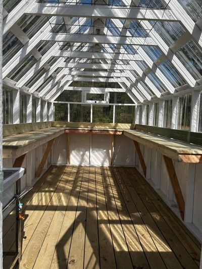 Greenhouse interior: Wraparound potting benches under clear panels.