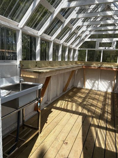 Greenhouse interior with a stainless utility sink and faucet beside a long potting bench