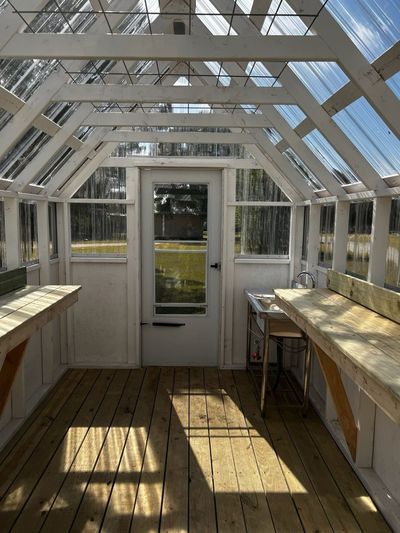 Looking toward the glass storm door inside a greenhouse, with benches on both sides
