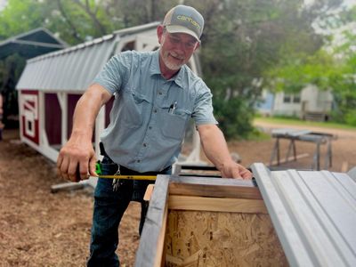 Measuring the top of a coop's frame at the Harmony shop, with finished coops behind