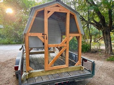 A white and natural barn coop strapped to the trailer in the early sun