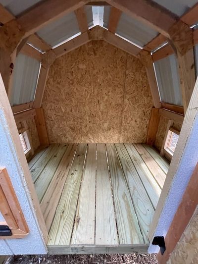 Inside a raised henhouse: Treated plank floor under a gambrel roof, with screened windows for airflow.